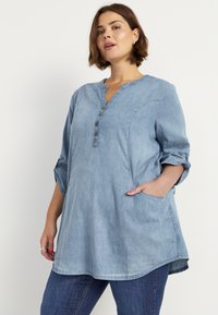 Hellblaues Denim-Tunika mit Notch-Kragen, vier Knöpfen, Dreiviertelärmeln und seitlichen Taschen, mit lockerer Passform und abgerundetem Saum.