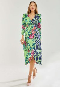 Floral and zebra-patterned wrap dress in green, featuring puff sleeves and a high slit, paired with pink heeled shoes.