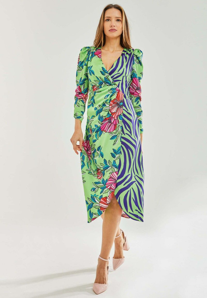 Floral and zebra-patterned wrap dress in green, featuring puff sleeves and a high slit, paired with pink heeled shoes.