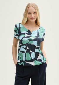 Haut court à manches courtes coloré présentant un mélange de motifs abstraits bleus, verts et noirs, avec un col boutonné et une coupe décontractée.