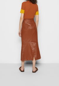Jupe midi en cuir synthétique marron avec un ourlet légèrement évasé et une fente décorative ; assortie à un haut marron à côtes et des accents de poignet jaunes.