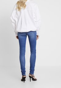 Blå skinny jeans, hög midja, något slitna detaljer på bakfickorna, kombinerat med en lös vit skjorta och svarta sandaler med remmar.