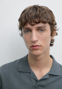 Model wearing a gray collared shirt, short sleeves, smooth texture, and subtle stripes, standing against a plain light background.