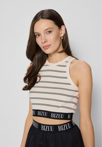 Jasno beżowy top typu crop z czarnymi poziomymi paskami, okrągłym dekoltem i paskiem z logo BIZUU. Noszony z czarną spódnicą o podobnym brandingiem.