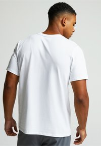 Valkoinen puuvillataka, jossa on lyhyet hihat ja pyöreä pääntie. T-paidassa on sileä pinta ja hieman rento istuvuus.