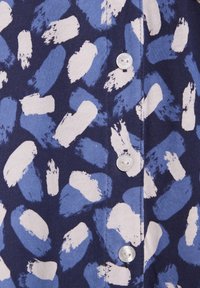 Tessuto blu navy con motivo astratto di pennellate bianche e azzurre, caratterizzato da una fila di bottoni rotondi lungo la parte anteriore.