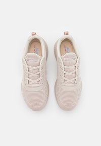 Ljusrosa träningsskor med en texturerad stickad ovandel, snörningsdesign, vadderad krage och en låg gummisula. Anmärkningsvärd logotyp på tungan.