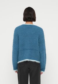 Μπλε αφράτο πουλόβερ με υφασμένο πλέξιμο, με ανοιχτό μπλε τελείωμα στο τελείωμα και τις μανσέτες, σχεδιασμένο με άνετη εφαρμογή και μακριά μανίκια.