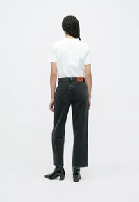 Blugi negri cu talie înaltă, croială dreaptă și două buzunare în spate, asortați cu un tricou alb simplu și cizme negre cu toc.