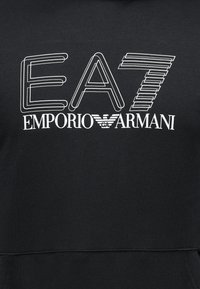 Svart hoodie med vit text "EA7 Emporio Armani" i ett modernt typsnitt och en kombination av fyllda och konturerade bokstäver.