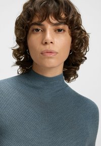 Rybkowany golf w stonowanym niebieskim kolorze, o dopasowanym kroju i delikatnej fakturze, z subtelnymi pionowymi wzorami przez całą powierzchnię.