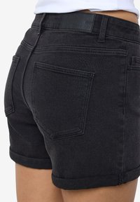 Juodi džinsiniai šortai su suvertais kraštais, pasižymintys lygiu tekstūrom, užpakalinėmis kišenėmis ir logotipo etikete ant juosmens.