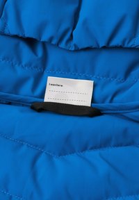 Tessuto imbottito blu con una superficie liscia. Presenta un'etichetta bianca con la dicitura "Ero qui:" e una cinghia nera per il fissaggio.
