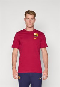 Rød bomulds T-shirt med et Barcelona-logo p�å venstre bryst og et gult Nike-swoosh. Korte ærmer, rund halsudskæring.