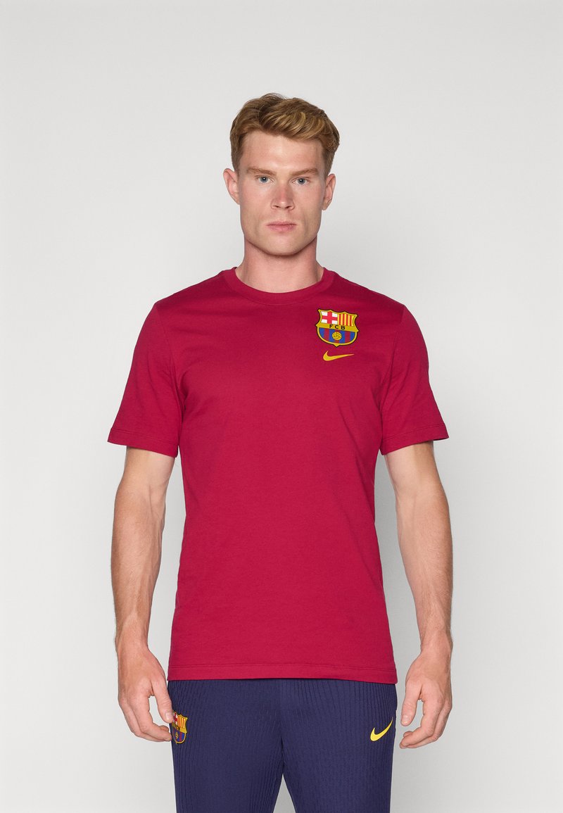 Punainen puuvillapaita, jossa vasemmassa rinnassa on Barcelona-logo ja keltainen Nike-swoosh. Lyhyet hihat, pyöreä kaula-aukko.