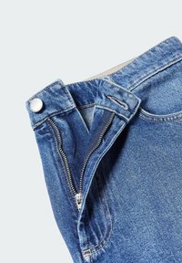 Jean en denim bleu avec une fermeture éclair ouverte et une braguette à boutons sur un fond clair uni.