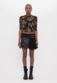 Fekete mintás crop top virágos mintával, fekete szoknyával kombinálva, bőr részletekkel és csattokkal. A megjelenést fekete katonai csizmák teszik teljessé.