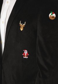 Svart blazer med broderade julteman: renhuvud, jultomte och julpudding, bärs över en vit skjorta.