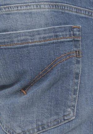 Tasca posteriore di jeans di denim blu con cuciture arancioni a contrasto e un piccolo ornamento metallico a forma di lettera nell'angolo superiore.