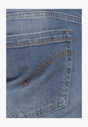 Tasca posteriore di jeans di denim blu con cuciture arancioni a contrasto e un piccolo ornamento metallico a forma di lettera nell'angolo superiore.
