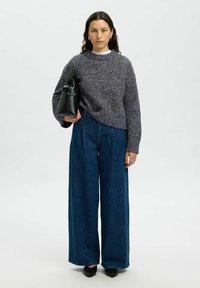 Sweter dzianinowy w ciemnoszarym kolorze z teksturowanym wzorem, sparowany z dżinsami o szerokich nogawkach w średnim niebieskim odcieniu. Czarna torebka na ramię.