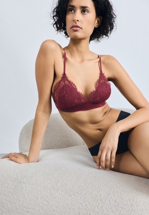 Bralette en dentelle bordeaux avec des bords délicats, des bretelles réglables et un slip bleu marine assorti, présentés sur un fond clair sur une surface texturée.