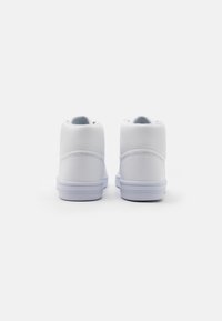 Un par de zapatillas altas blancas mostradas desde la parte trasera sobre un fondo blanco liso, destacando sus cuellos acolchados y suelas de goma.