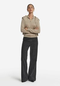 Beige långärmad polo skjorta lager på lager med en tröja, i kombination med högmidjade mörka jeans med vida ben och svarta skor.