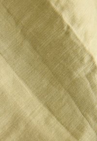 Gros plan sur un tissu beige avec une étiquette tissée subtile affichant un texte en relief pâle et une texture fine.
