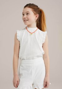 White sleeveless top with ruffled shoulders and a gathered neckline, paired with white shorts featuring a frilled hem. An orange bead necklace adds detail.
