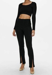 Svart långärmad crop top med rund halsringning, kombinerad med högmidjade svarta byxor med slitsar vid vristerna.