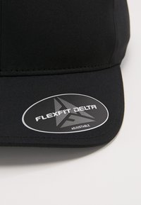 Crna kapa izrađena od glatkog materijala, sa zakrivljenim vizirima i podesivim trakama. Uključuje oznaku s natpisom "FLEXFIT DELTA" s logotipom.