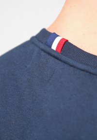 Marinblå t-shirt tyg med en slät textur, med en nacketikett i blå, vit och röda ränder för detaljaccent.