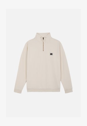 Jersey beige de manga larga con cremallera de un cuarto y pequeño parche con el logo de un oso negro en el pecho izquierdo, puños y bajo acanalados.