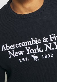 Maglione a maglia blu scuro con colletto a costine. Presenta la scritta bianca ricamata "Abercrombie & Fitch, New York, N.Y." e un logo alce.