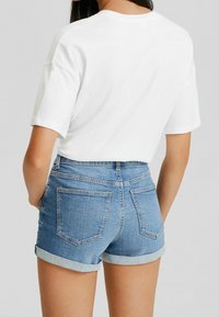 Ljusblå denimshorts med upprullade fållar, två bakfickor och hög midja, i kombination med en enkel vit t-shirt.
