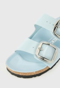 Svijetloplave sandale s dva široka remena, srebrnim kopčama i pluta nogu. Potplat je crn s teksturiranim završetkom.