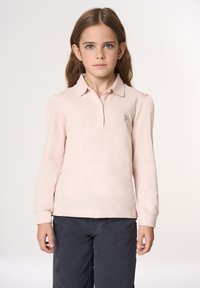 Polo a maniche lunghe di colore rosa pallido con colletto classico, abbottonatura e logo ricamato. Abbinato a pantaloni scuri, presenta una texture morbida.