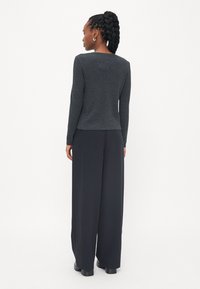 Dark gray fitted sweater with long sleeves, paired with loose black trousers. Smooth texture with a subtle knit pattern.
