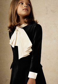 Melnas samta kleita ar garām piedurknēm, kas ir aprīkota ar lielu krēmkrāsas tauriņu pie kakla un baltām aproču detaļām. Gluda tekstūra ar elegantu dizainu.