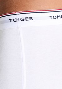 Taille- en heupgebied van een persoon die witte Tommy Hilfiger ondergoed draagt met een elastische tailleband in rood, wit en blauw.