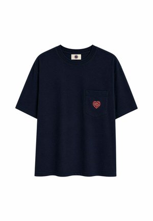 Camiseta negra de manga corta con cuello redondo y un bolsillo delantero con un pequeño parche en forma de corazón rojo con texto.