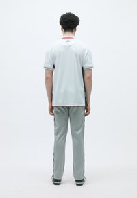 Conjunto desportivo com uma camisola de mangas curtas branca com detalhes verdes e calças cinzentas. Inclui um pequeno logótipo e riscas laterais com padrão.