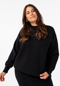 Schwarzer, übergroßer Pullover aus weichem Material mit geripptem Halsausschnitt und Saum. Verfügt über eingesetzte Schultern und lange Ärmel.