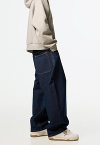 Lösa mörkblå denimjeans med rak benpassform, har en bakficka och subtila sömnadsdetaljer, tillsammans med vita sneakers.