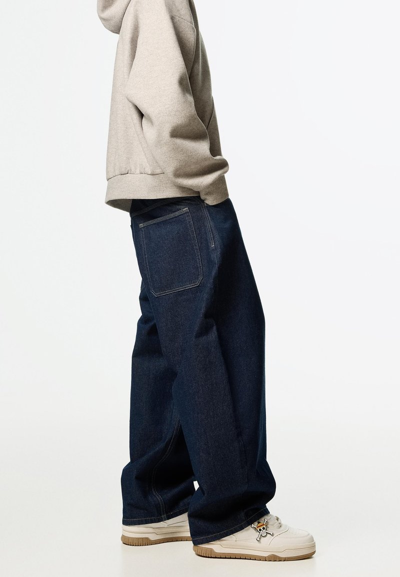 Lösa mörkblå denimjeans med rak benpassform, har en bakficka och subtila sömnadsdetaljer, tillsammans med vita sneakers.