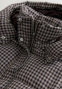 Brūns un zils raibais mīkstais džemperis ar augstu apkakli, priekšējo rāvējslēdzēju un pogu aizdari, ar teksturētu audumu un iekšējo oderi.