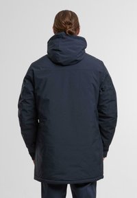 Giacca isolante blu navy con cappuccio, caratterizzata da una texture liscia, maniche lunghe e un orlo leggermente curvo. Include tasche laterali con zipper.