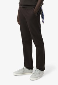 Bruine broek van gladde stof, met zijzakken en een relaxed fit. Gecombineerd met lichtgrijze sneakers en een gestreepte sjaaldetail.
