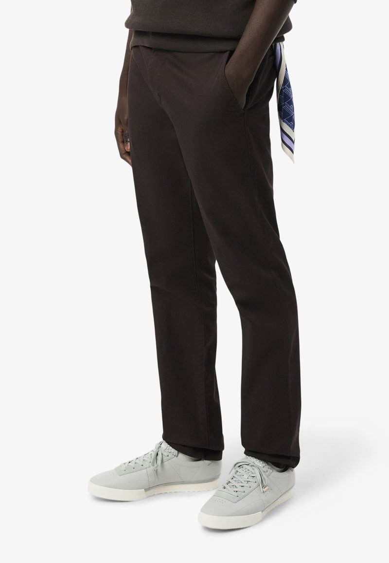 Bruine broek van gladde stof, met zijzakken en een relaxed fit. Gecombineerd met lichtgrijze sneakers en een gestreepte sjaaldetail.